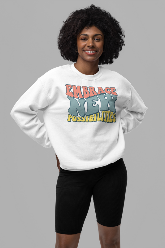 A person wearing the Sharp Tact Kreativ "Embrace New Possibilities Sweatshirt," featuring colorful lettering on a white fleece knit fabric, stands against a plain gray background, highlighting its unisex sizing.