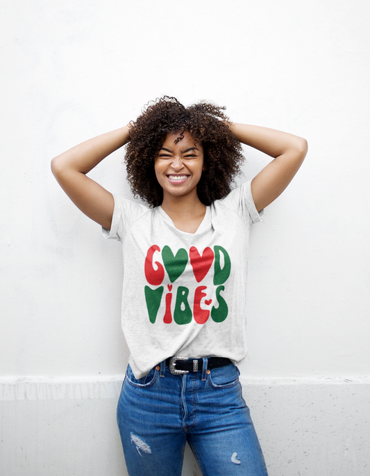 A young woman wearing jeans and a Good Vibes Holiday Tee from Sharp Tact Kreativ | Tees & Gifts with Encouraging Messages to Brighten Your Day with a Bit of Wit.