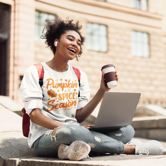 A woman sitting on the steps with a laptop and a cup of coffee, wearing a Sharp Tact Kreativ Pumpkin Spice Season Sweatshirt embraced by the fall season vibes as she enjoys her pumpkin spice-flavored drink.